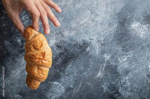 Hand holding a delicious croissant on a gray background