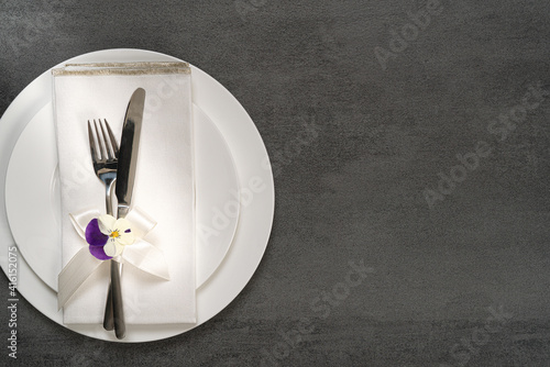 Beautiful rustic feminine wedding or birthday table setting on grey background..White porcelain ,cutlery,napkin and flowers.Flat lay, top view with copy space.