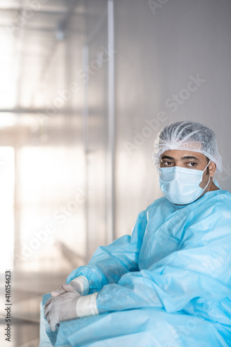 Exhausted male surgeon in protective workwear leaning against wall in corridor