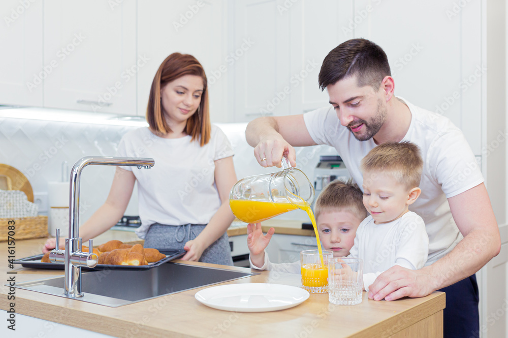 Young happy family with two young sons preparing breakfast together in their kitchen Young happy family with two young sons preparing breakfast together in their kitchen