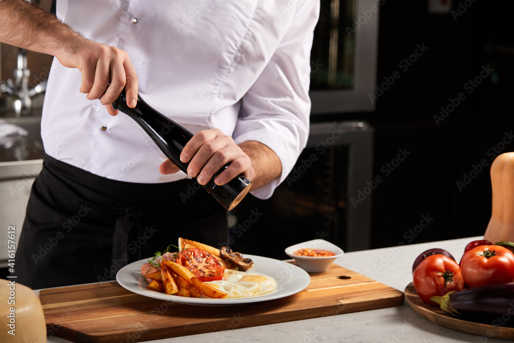 Professional Chef-cook Decorating Dish In Restaurant Kitchen Alone. Man In White Apron Makes Finishing Touch On DIsh. Culinary, Restaurant, Gourmet Concept