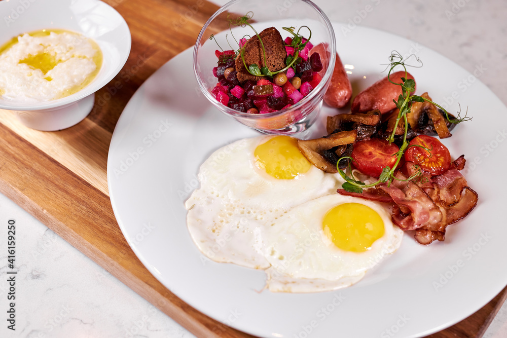 Fried Eggs With Bacon, Tomato and Salad Served At Cafe Table On Wooden Board , English Breakfast. Food, Restaurant concept Fried Eggs With Bacon, Tomato and Salad Served At Cafe Table On Wooden Board , English Breakfast. Food, Restaurant concept