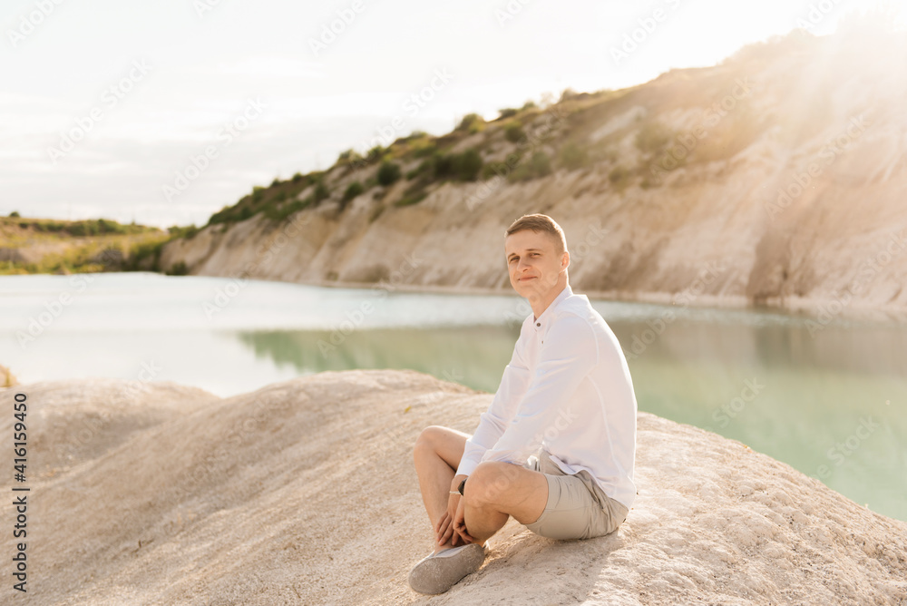 Beautiful young guy travels the world near a blue lake and sand at sunset