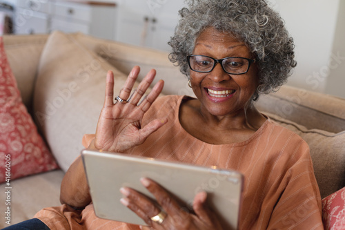 African american senior woman smiling and waving while having a video call on digital tablet at home