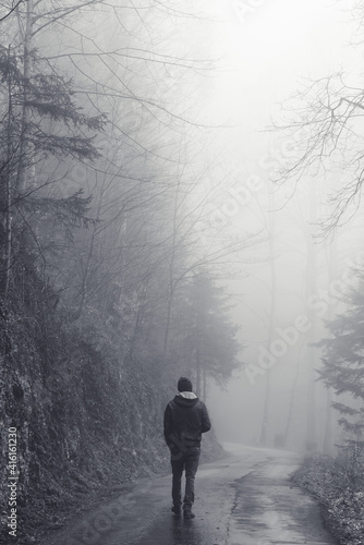 Man walking alone on a road through a dark foggy forest