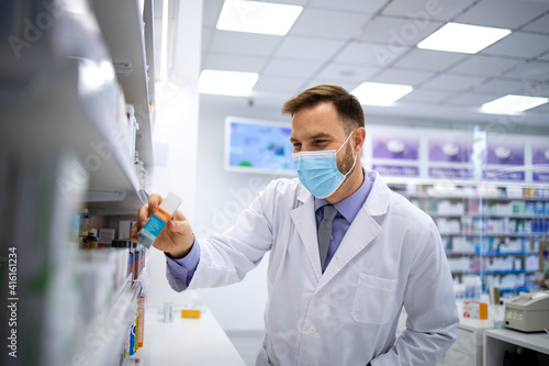 Foto Pharmacist wearing face mask and white coat choosing appropriate vitamins in pharmacy store to sell to the customer during corona virus pandemic