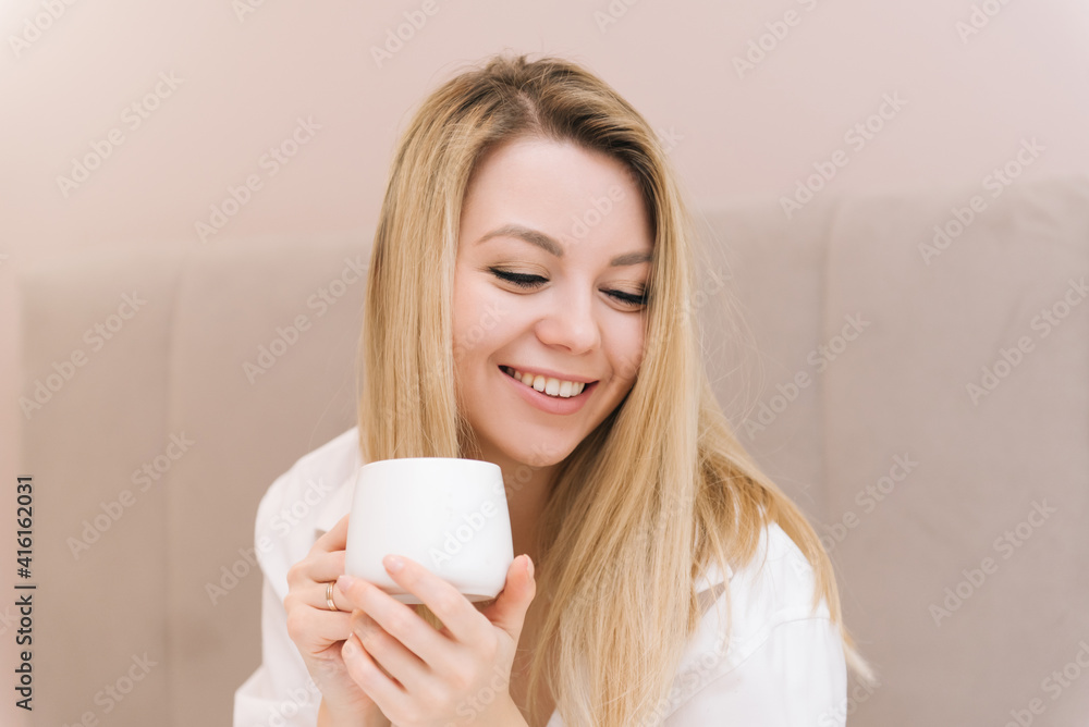 Beautiful young blonde smiling girl with coffee in a white bed, good morning Beautiful young blonde smiling girl with coffee in a white bed, good morning