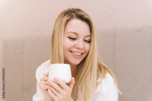 Beautiful young blonde smiling girl with coffee in a white bed  good morning