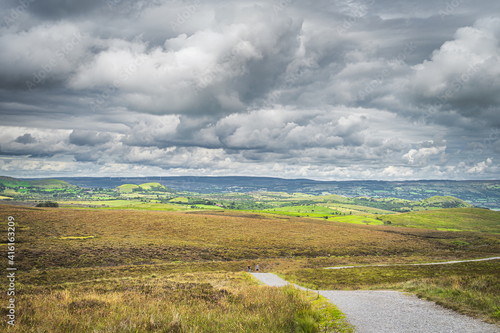 Tourists walking between green hills and peatbog with stormy, dramatic sky in background, Cuilcagh Mountain Park, Northern Ireland
