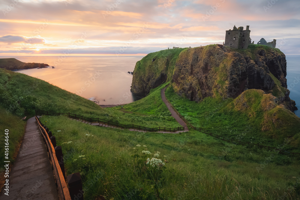 Golden sunrise or sunset light on the coastal landscape ruins of Donnottar Castle on the Aberdeenshire coast of Scotland.