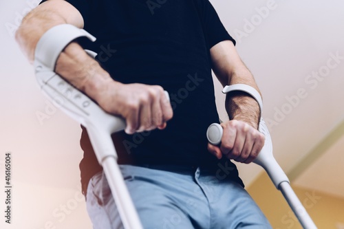 Disabled man using crutches to walk. Rehabilitation of a broken leg at home.
