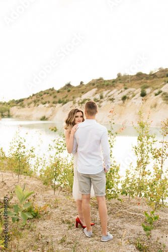 A beautiful young couple in love, a man and a woman embrace, kiss near a blue lake and sand at sunset. Vacation at the sea on the beach, sunset, morning, honeymoon, tropics, ocean, girl, relationship. © ksyusha_yanovich