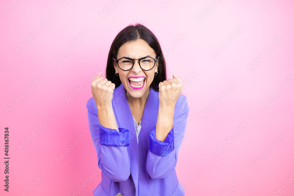 Φωτογραφία Young business woman wearing purple jacket over pink background very happy and excited making winner gesture with raised arms, smiling and screaming for success