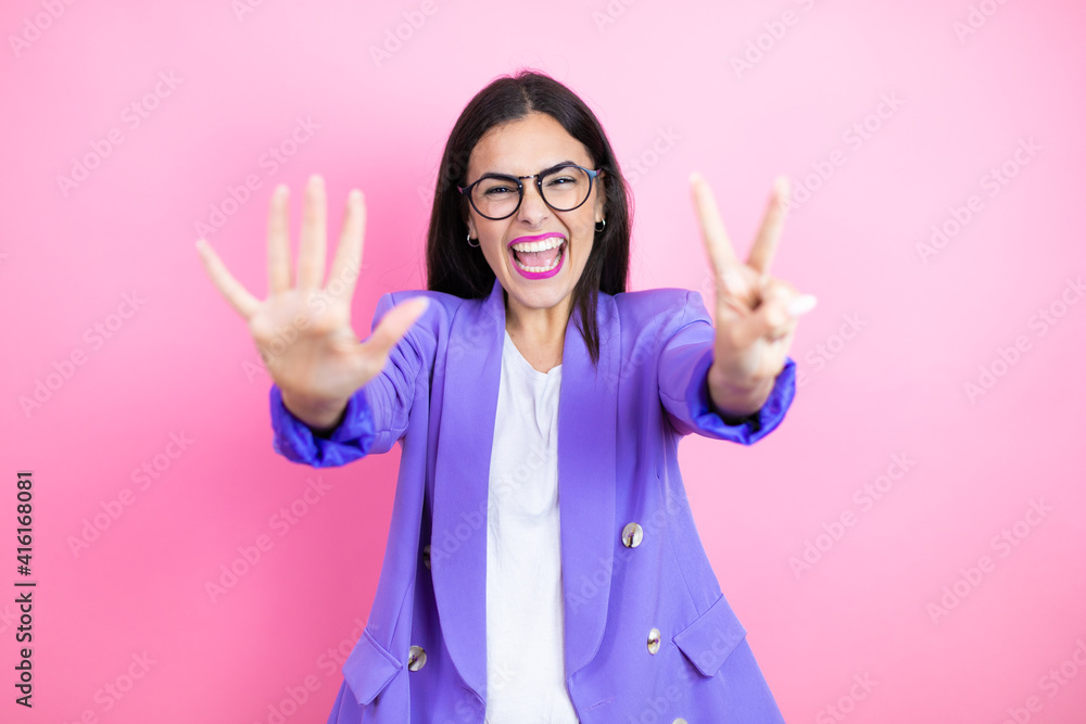 Young business woman wearing purple jacket over pink background showing and pointing up with fingers number seven while smiling confident and happy Young business woman wearing purple jacket over pink background showing and pointing up with fingers number seven while smiling confident and happy