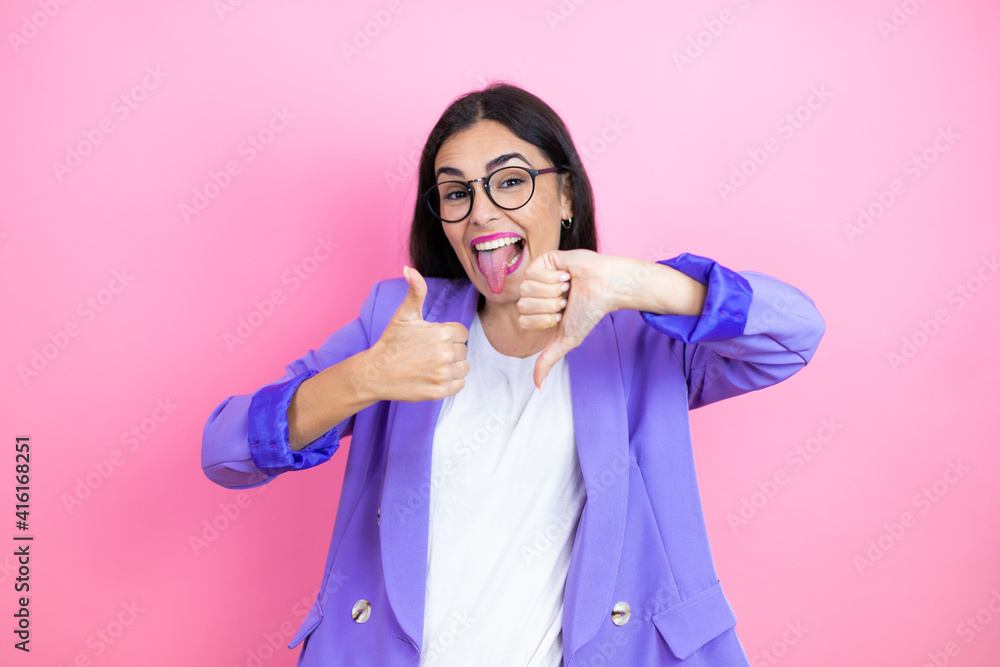 Young business woman wearing purple jacket over pink background Doing thumbs up and down, disagreement and agreement expression. Crazy conflict Young business woman wearing purple jacket over pink background Doing thumbs up and down, disagreement and agreement expression. Crazy conflict