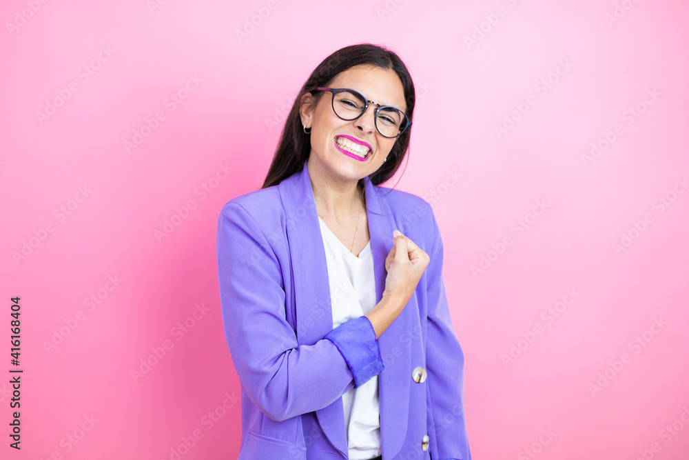 Young business woman wearing purple jacket over pink background feeling happy, positive and successful, motivated when facing a challenge or celebrating good results Young business woman wearing purple jacket over pink background feeling happy, positive and successful, motivated when facing a challenge or celebrating good results