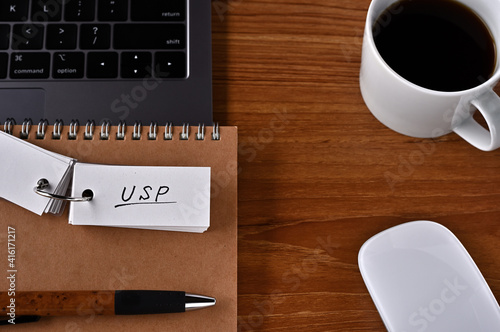 On the desk there is a laptop  a cup of coffee  and a word book with the word USP written on it. It was an abbreviation for the financial term Unique Selling Proposition.