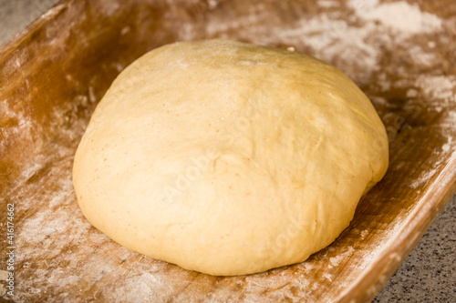 Ball of risen monkey bread dough ready for making balls out of, resting in an antique bread or dough trough.
