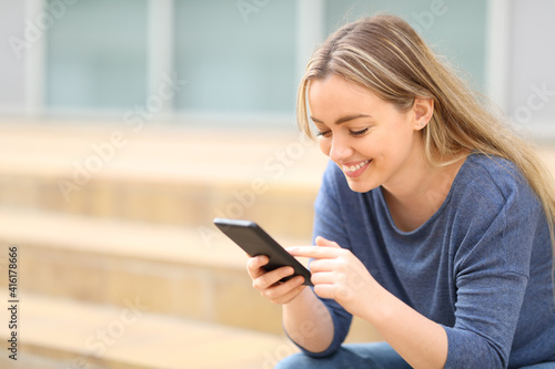 Happy teen checking smart phone in the street