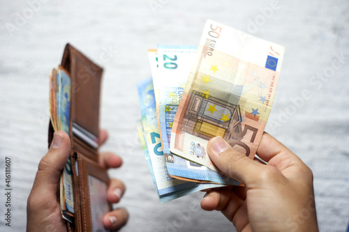 man's hands opening wallet and taking out banknotes. person counting euro banknotes of 50, 20 and 10 euros. colored bolletes, with brown hands and brown leather wallet