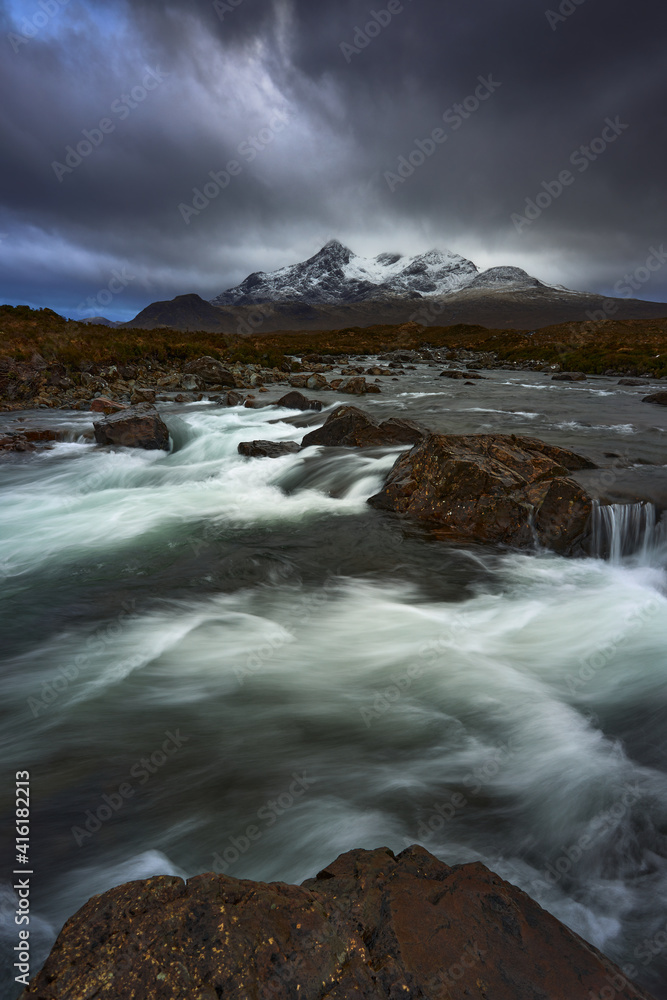 Dramatic sky over large mountains from the River Sligachan on the Isle of Skye Scotland with the Cuillin mountain range in the distance with snow in winter, Isle of Skye, Scotland