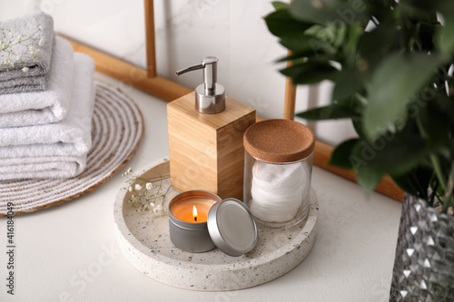 Tray with soap dispenser, cotton pads and burning candle on countertop in bathroom