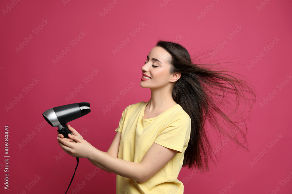Beautiful young woman using hair dryer on pink background Beautiful young woman using hair dryer on pink background