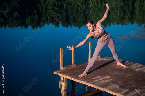Young woman on wooden pier above forest lake scenery, folds her arms in a namaste gesture. Woman arms outstretched in nature.