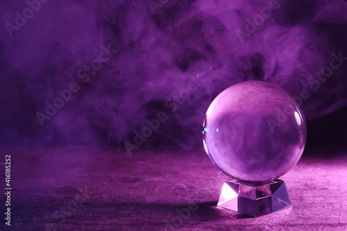 Crystal ball on table and smoke against dark background, space for text. Predictions of future