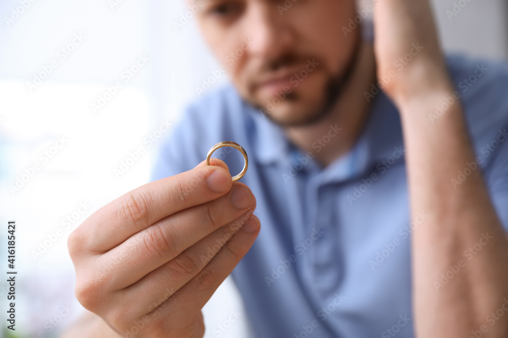 Fototapeta premium Man holding wedding ring on light background, closeup. Divorce concept
