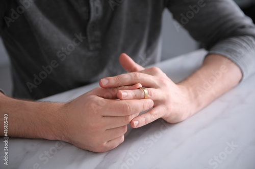 Man taking off wedding ring at white marble table, closeup. Divorce concept