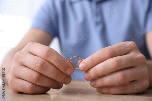 Man holding wedding ring at wooden table  closeup. Divorce concept