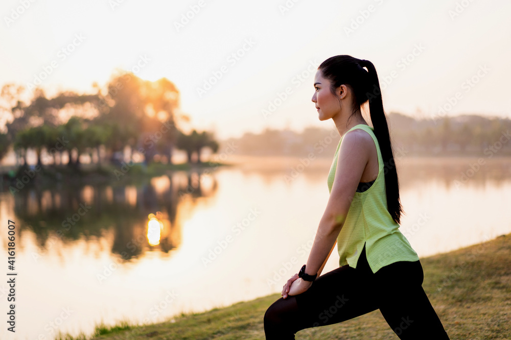 A young Asian female workout before a fitness training session at the park under sunlight in the morning. Healthy young woman warming up outdoors. Sport and recreation
