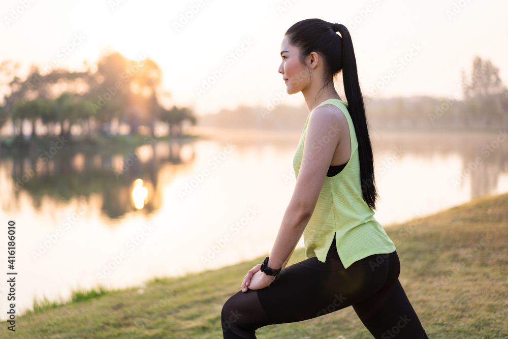 A young Asian female workout before a fitness training session at the park under sunlight in the morning. Healthy young woman warming up outdoors. Sport and recreation