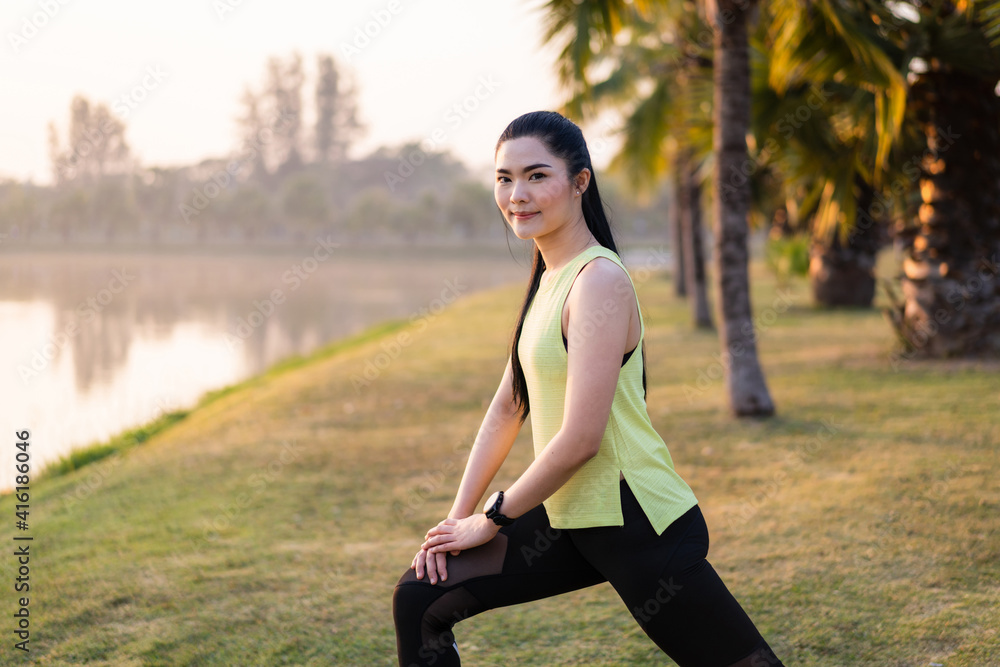 A young Asian female workout before a fitness training session at the park under sunlight in the morning. Healthy young woman warming up outdoors. Sport and recreation