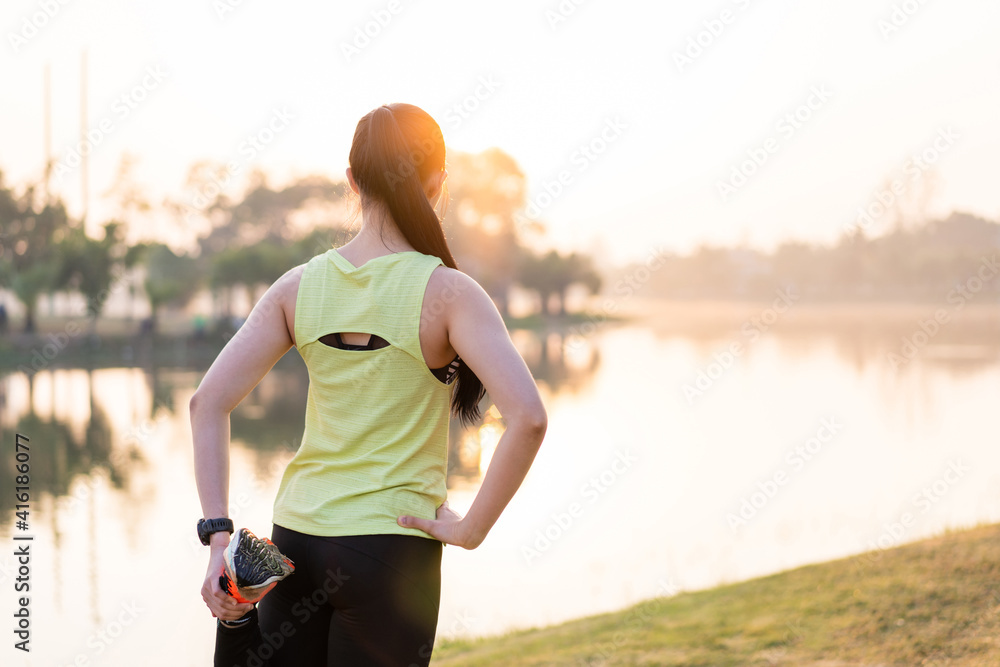Fototapeta premium A young Asian female workout before a fitness training session at the park under sunlight in the morning. Healthy young woman warming up outdoors. Sport and recreation