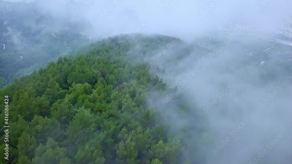 Aerial forward shot of clouds over dense forests and distant towns Aerial forward shot of clouds over dense forests and distant towns