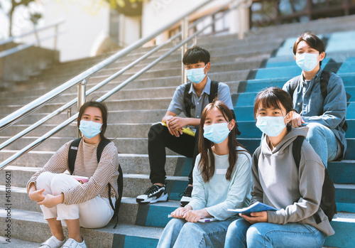young students wearing with face masks and sitting on the stairs