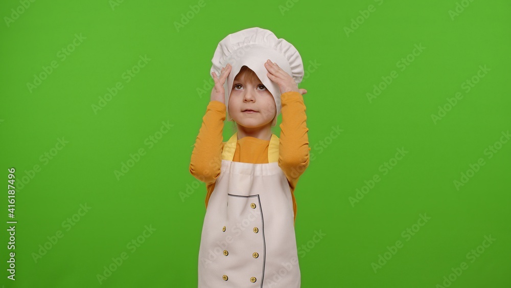 Child girl kid dressed as professional cook chef smiling, crosses arms and looks intently at camera on chroma key background. Nutrition, cooking school, education, food. Fun and humor. Copy-space Child girl kid dressed as professional cook chef smiling, crosses arms and looks intently at camera on chroma key background. Nutrition, cooking school, education, food. Fun and humor. Copy-space