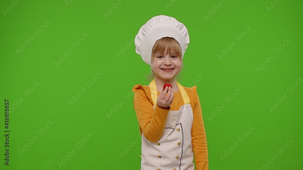 Little charming child girl dressed in apron like chef cook eats delicious fresh strawberries and laughing out loud on chroma key background. Nutrition, family cooking school, children education Little charming child girl dressed in apron like chef cook eats delicious fresh strawberries and laughing out loud on chroma key background. Nutrition, family cooking school, children education