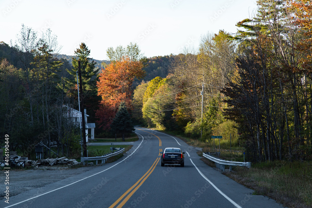 Fototapeta premium Car driving down a country road with autumn leaves in the background