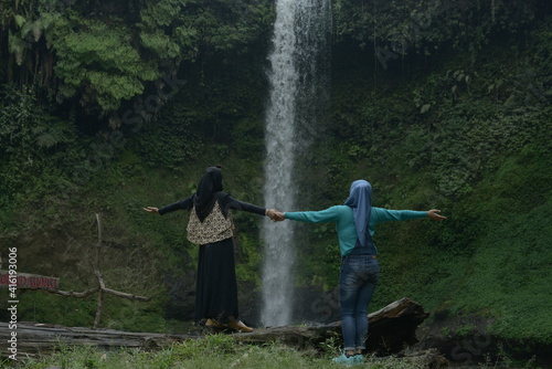 seen from behind two travelers with a waterfall background