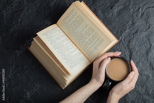 Woman hands holding a cup of coffee with book on a dark background photo