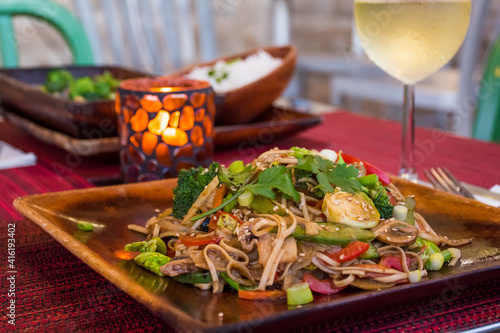 Healthy vegan Pad Thai served on a wooden plate in a relaxed environment. The meal is accompanied with a glass of white wine