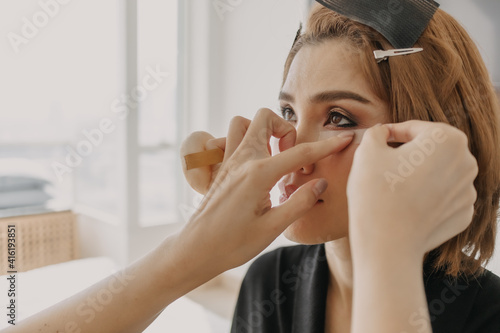 Asian woman is wearing makeup by the makeup artist.