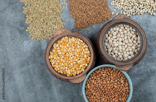 Different kinds of bean seeds, lentil, peas in dishes on a dark background