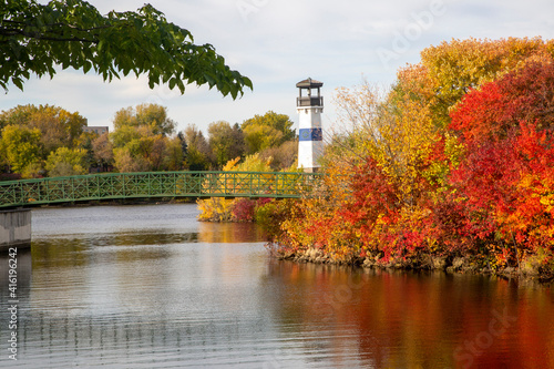 Beautiful autumn scene of a lighthouse on the river shore with trees turning red, yellow, and orange