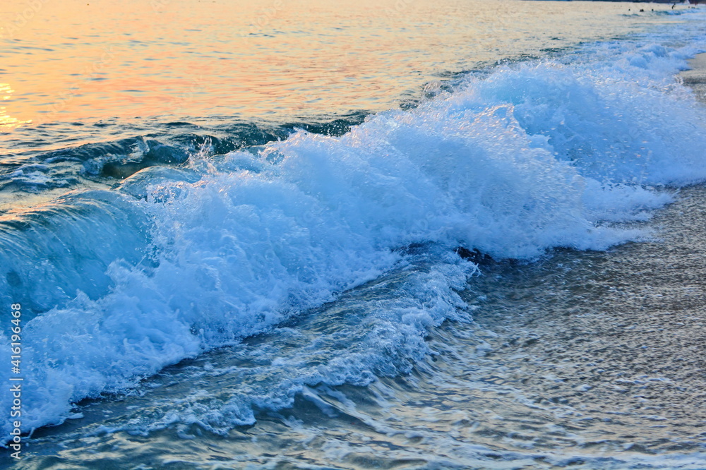Fototapeta premium Sunset on sea beach, waves and surf with white foam on wet sand. Horizontal frame