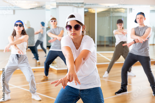 Teenage girl hip hop dancer in casual clothes, cap and sunglasses exercising with friends at dance center