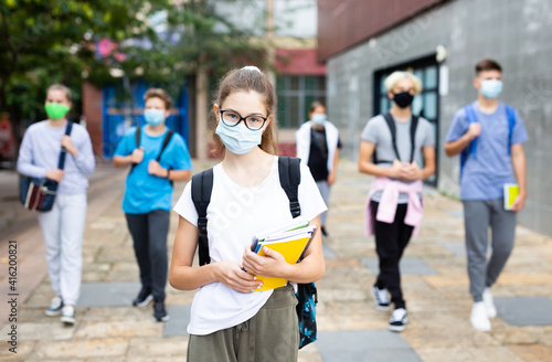 Portrait of teen girl student in face mask on her way to college in warm autumn day. Forced precautions in COVID pandemic.
